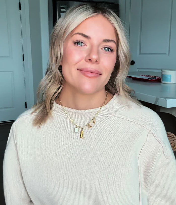 Blonde woman smiling in a cozy sweater indoors, representing Mormon soft-swinging parties discussion in a casual setting.