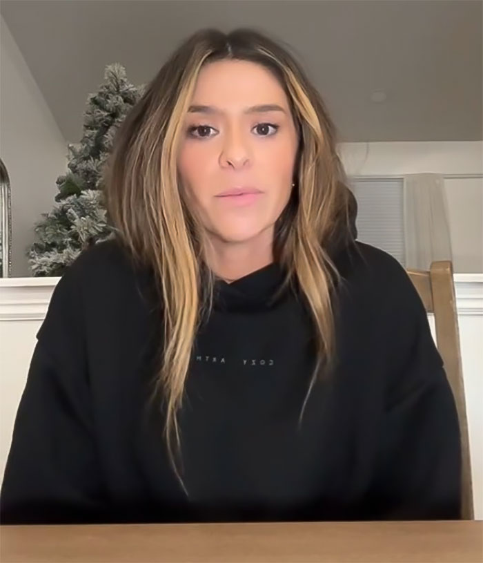 Woman with long hair in a black hoodie speaking about Mormon soft-swinging parties controversy indoors.