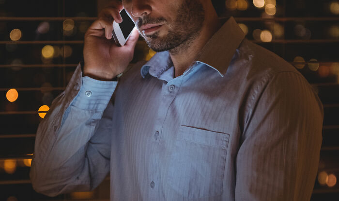 Man in a blue shirt talking on a phone, with city lights in the background, related to wild wedding events.