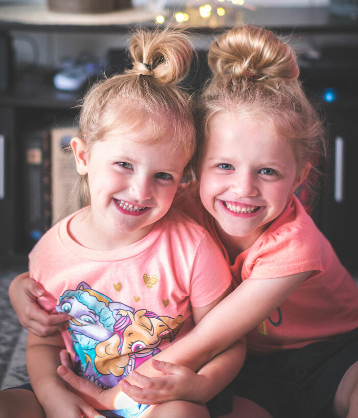 Two smiling children with top buns and matching peach shirts, captured in a cheerful home setting.