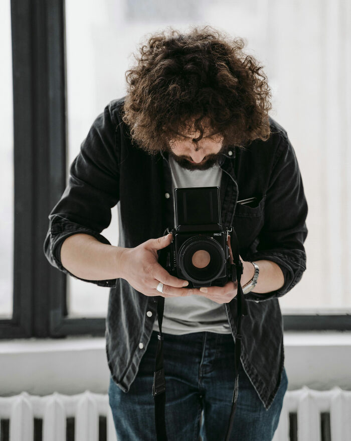 Person in a dark shirt using a vintage camera in a bright room, highlighting unusual moments.