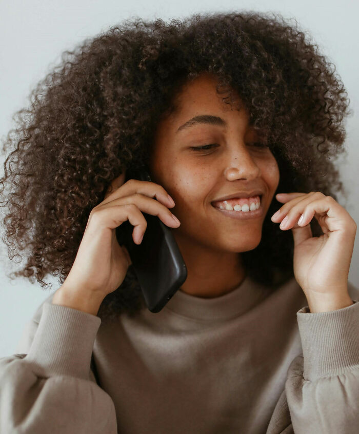 Smiling person with curly hair talking on a phone, illustrating the concept of dumb questions.