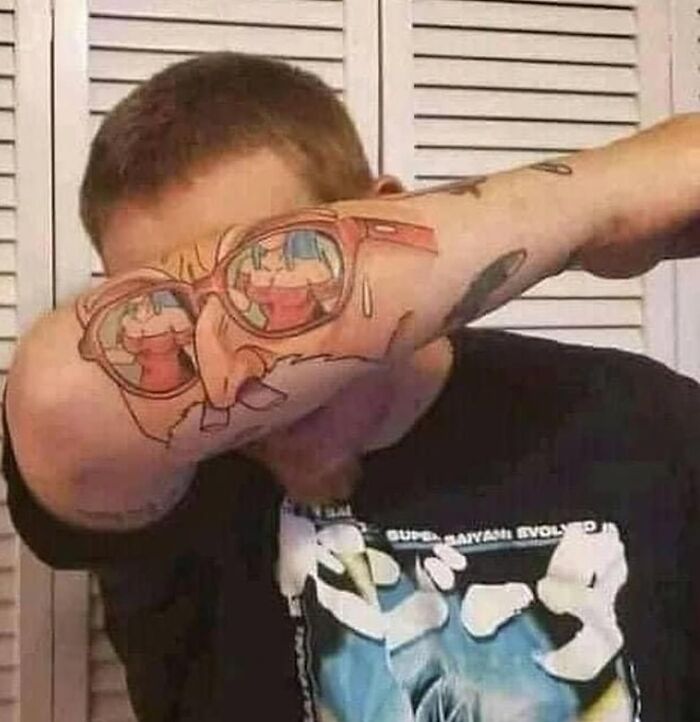 Man showing off epic tattoo fail on his arm, with cartoon face and glasses.