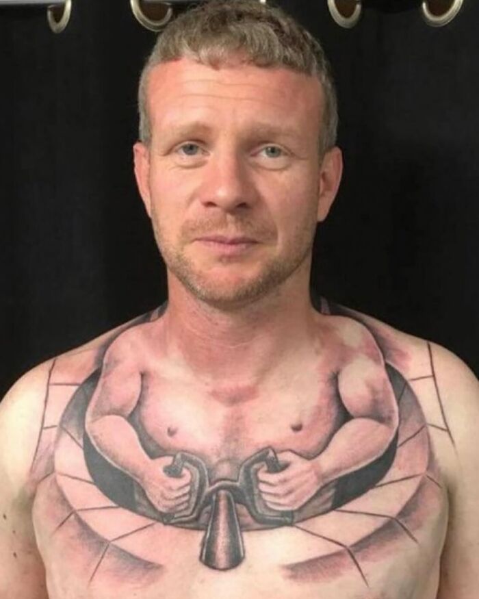 Man with tattoo fail depicting a muscular figure holding handles on his chest.