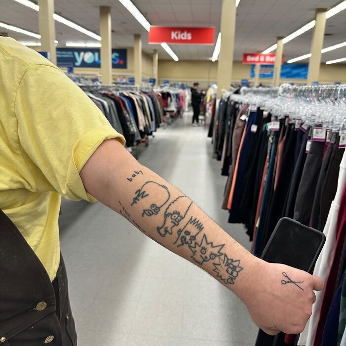 Arm with tattoo fail showing cartoon characters in a clothing store aisle.