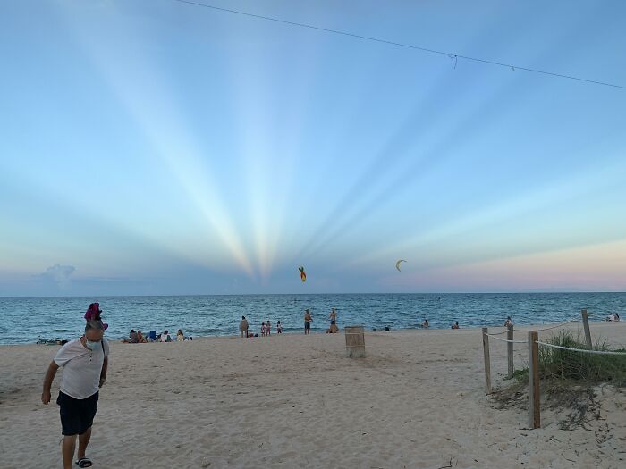 Sunset on a beach with people, showcasing a quirky optical phenomenon in the sky.