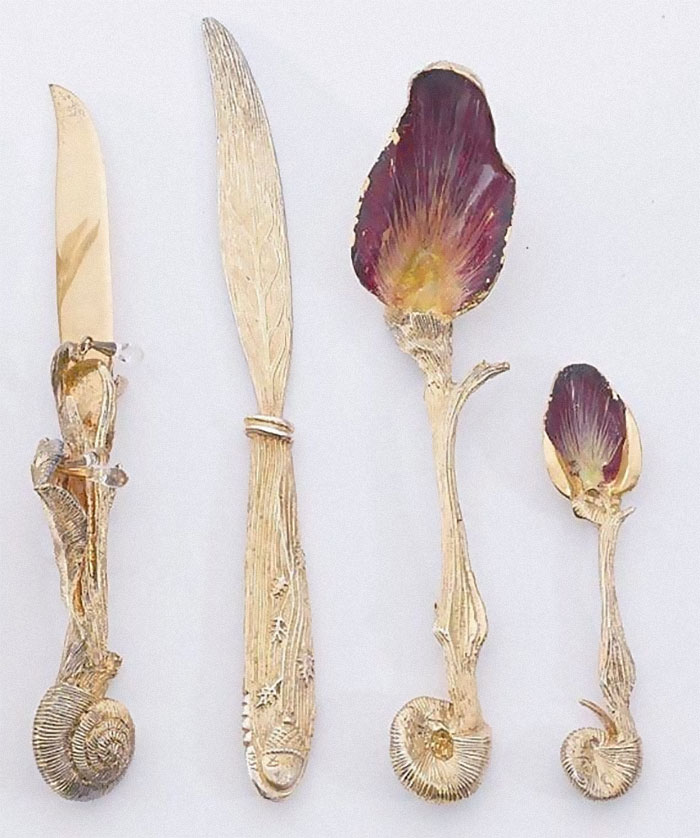 Set of ornate gold utensils with detailed floral and snail designs, a perfect example of designers creating hard-to-clean objects.