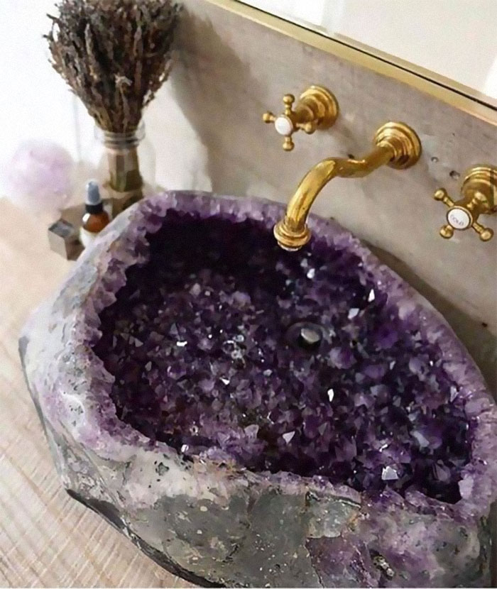 Amethyst crystal sink with rough edges and gold faucet, showcasing unique designer creation that is hard to clean.