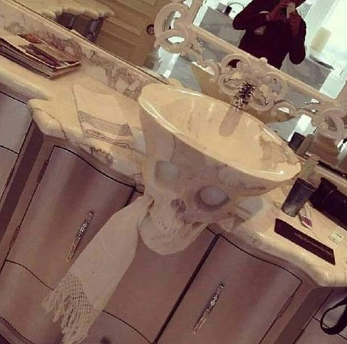 Bathroom sink shaped like a skull with a towel hanging from its mouth, an example of design that will need frequent cleaning.