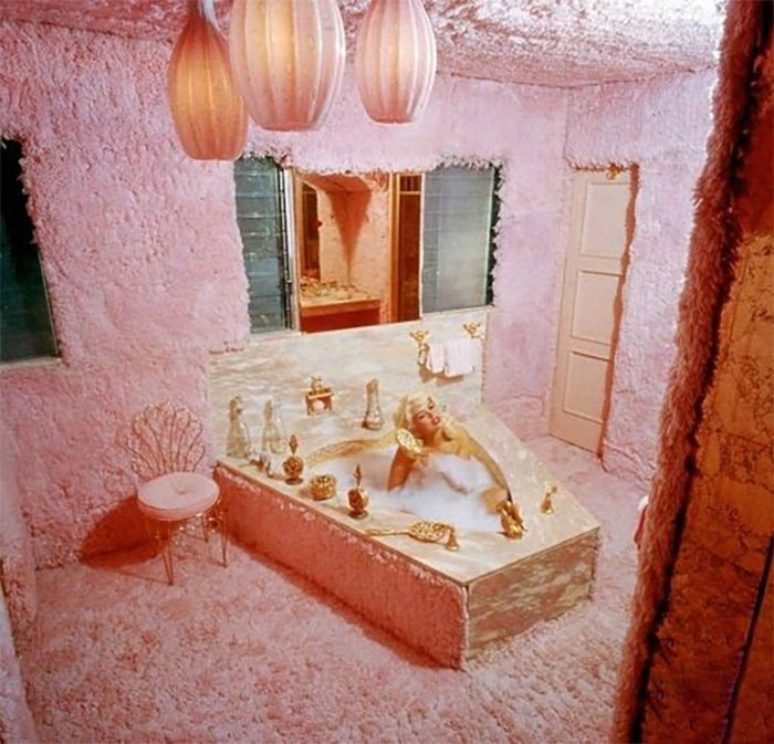 Bathroom covered in thick pink carpet with a bathtub and gold fixtures, showcasing a challenging cleaning design by designers.