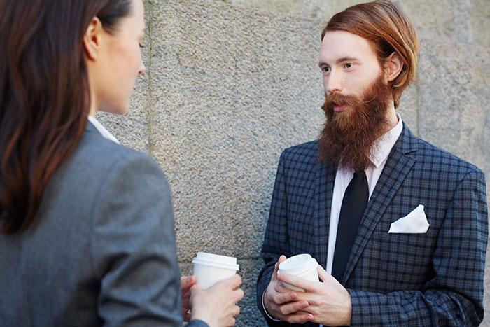 Two office colleagues in conversation, holding coffee cups, wearing business attire near a wall. Two office colleagues in conversation, holding coffee cups, wearing business attire near a wall.
