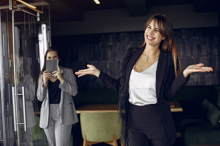 Office joke around boss as she gestures confidently, with a colleague holding a tablet in the background. Office joke around boss as she gestures confidently, with a colleague holding a tablet in the background.