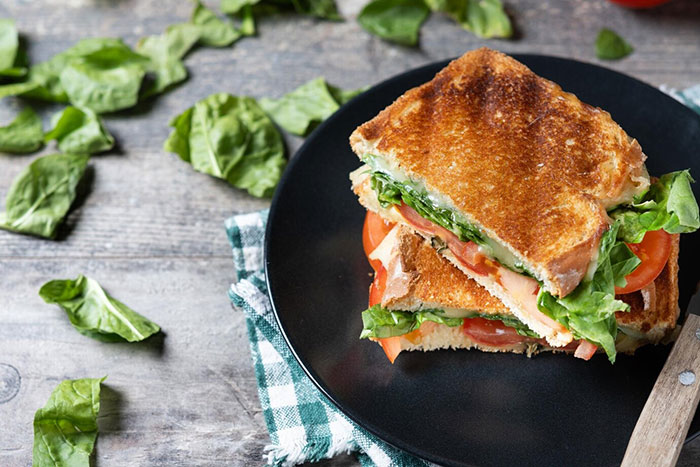 Grilled sandwich with lettuce and tomatoes on a black plate, garnished with fresh spinach leaves. Grilled sandwich with lettuce and tomatoes on a black plate, garnished with fresh spinach leaves.