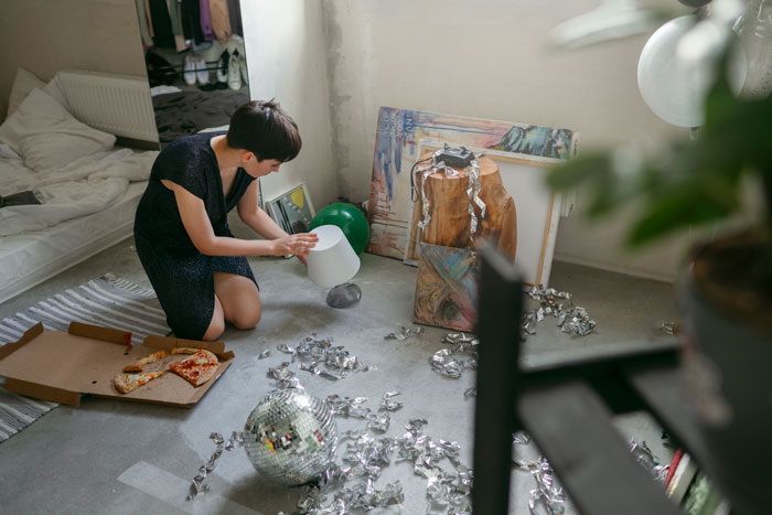 Young adult finds room trashed, kneeling among scattered belongings and debris, examining a lamp. Young adult finds room trashed, kneeling among scattered belongings and debris, examining a lamp.