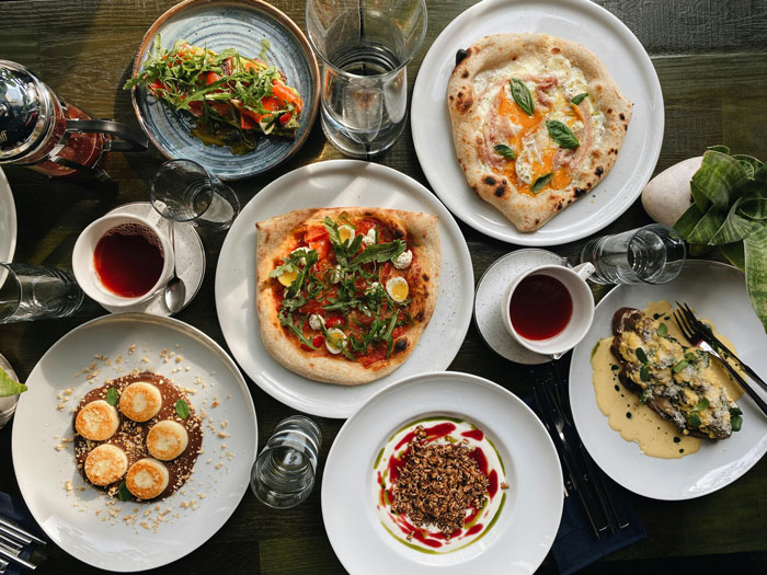 A variety of gourmet meals on a table, including pizzas, salads, and desserts, reflecting a shared dining experience. A variety of gourmet meals on a table, including pizzas, salads, and desserts, reflecting a shared dining experience.