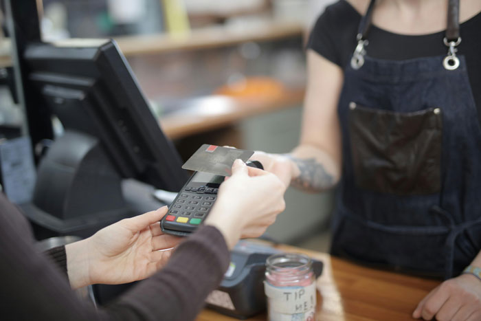 Customer paying with card at a café counter, depicting an added fee situation. Customer paying with card at a café counter, depicting an added fee situation.