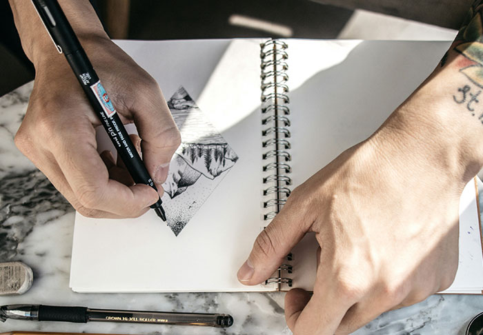 Person designing tattoo in notebook; meme inked on woman's skin as first tattoo mistake.