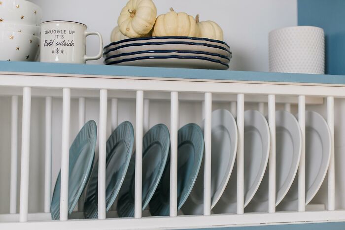 "Obsolete luxury home feature: plate rack displaying blue and white dishes, with mugs and pumpkins on top shelf."