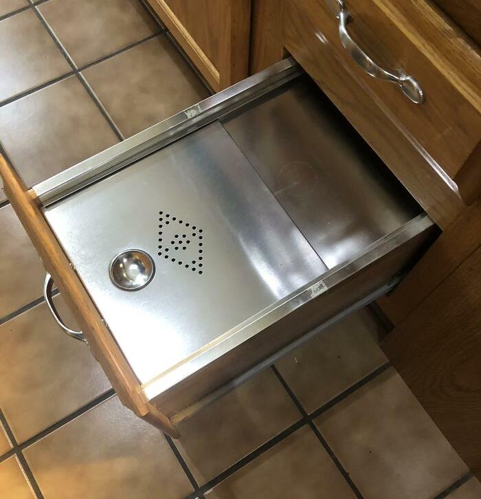 Obsolete luxury: Vintage metal warming drawer in a wooden kitchen cabinet with tiled floor.