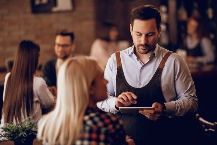 Waiter taking orders in a busy restaurant setting, illustrating things that might make people upset in hospitality environments.