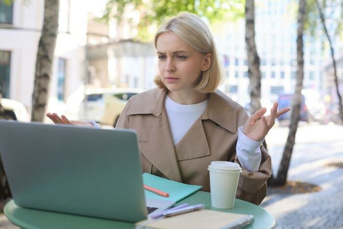 Woman looking frustrated at a laptop in a cafe, capturing the essence of things that make people dislike others.