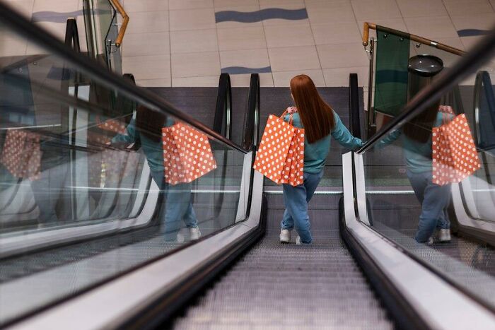 Person on escalator holding large polka dot shopping bag, possibly representing things people find annoying in public spaces.