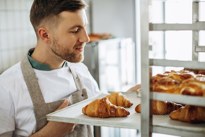 Man with a baking apron holding a tray of croissants, illustrating a risky decision in culinary pursuits.
