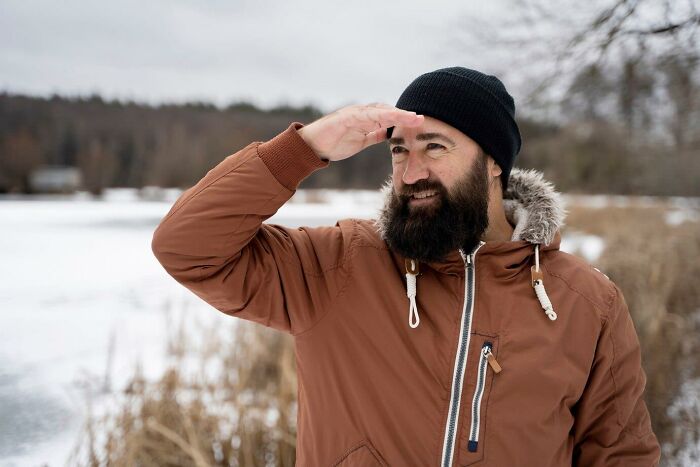 Man in winter coat and beanie making a risky decision outdoors, overlooking a snowy landscape.