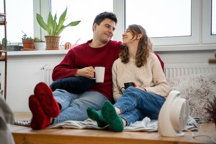 A couple sitting together, smiling, holding mugs, and wearing cozy knitted socks, symbolizing risky decision outcomes.