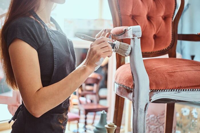 Person painting a vintage chair white, representing a risky decision in DIY furniture restoration.