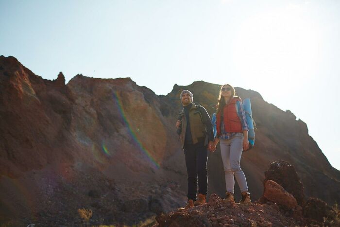 Couple hiking on a rocky mountain trail under bright sunlight, enjoying a risky adventure.