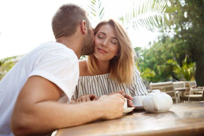 A man kissing a smiling woman's cheek at an outdoor cafe, representing a risky decision moment.