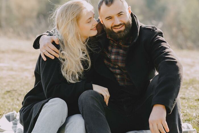A couple sitting outdoors, smiling and embracing, enjoying a risk-taking moment together.