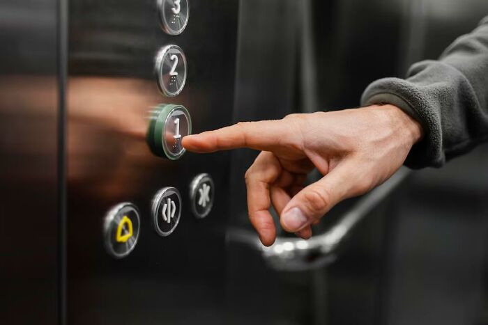 A hand pressing an elevator button, capturing a moment of reverse culture shock experienced by Americans lived abroad.