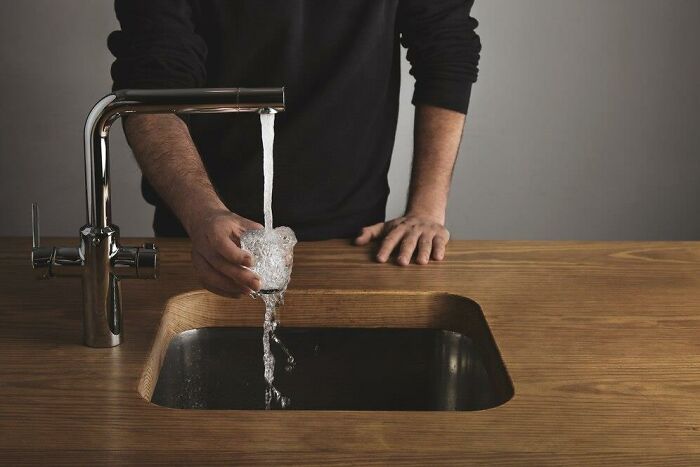 Person experiencing reverse culture shock while filling a glass at a modern kitchen sink.
