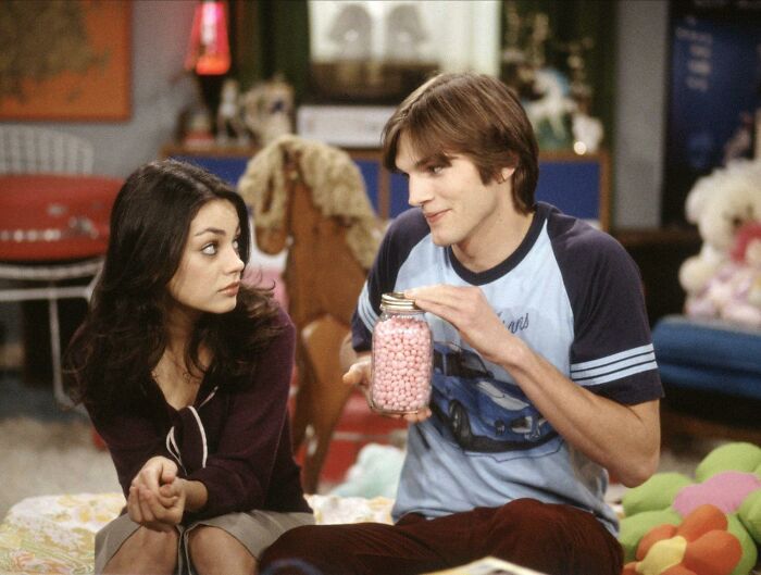 Two people on a sitcom set, with one holding a jar of candy, in a scene related to celebrities.