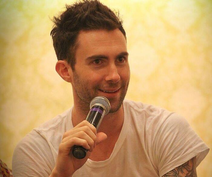 Person holding a microphone, smiling in a white shirt.