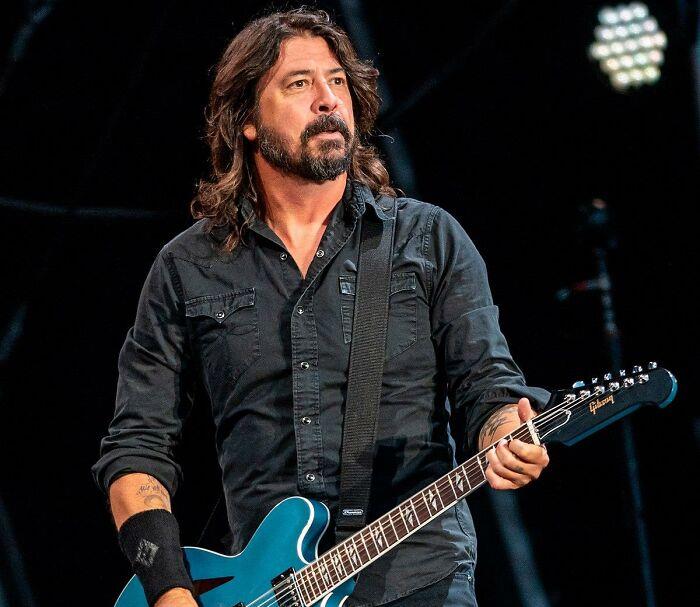 Musician with long hair playing a blue electric guitar on stage.