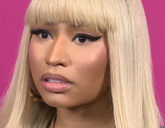 Blonde-haired celebrity with dramatic eyeliner against a pink background.