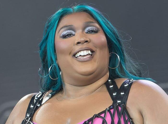 Singer performing on stage with glittery makeup, wearing a black and pink outfit, smiling amidst a vibrant atmosphere.