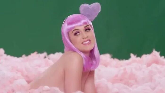 Person with pink hair and a heart headpiece among cotton candy clouds, smiling against a green background. Keywords: celebrities lost respect.