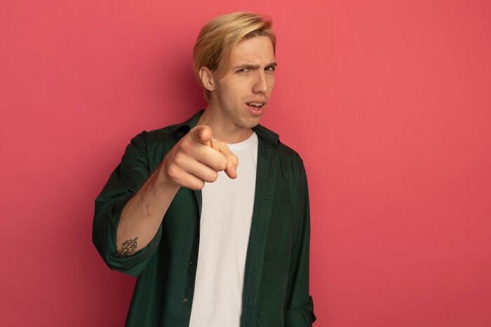 Person pointing with a skeptical expression, highlighting societal double standards in a pink background setting.