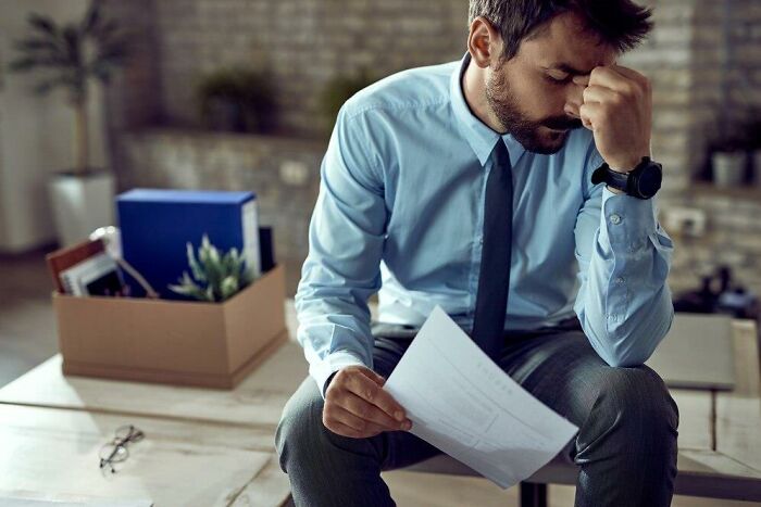 Man in office attire looking stressed, holding a paper, representing societal double standards.