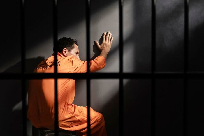 Man in an orange jumpsuit sitting in a cell, illustrating societal double standards.