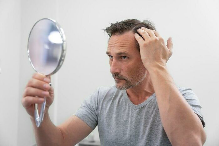 Man checking hair health in mirror, concerned about low iron levels affecting vegan diet decisions.