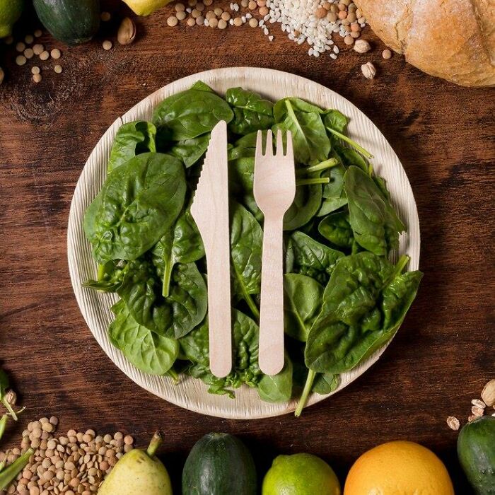 Plate of spinach with wooden cutlery, highlighting vegan food and iron levels.