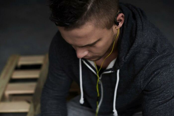 Young man in a hoodie listening to music with earphones, sitting thoughtfully, related to low iron levels and veganism.