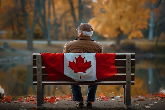 Elderly man sitting on a bench with a Canadian flag, autumn background, reflecting on what scares people in his country.