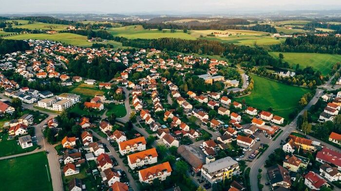 Aerial view of a small countryside town with red-roofed houses and green fields, representing a serene rural landscape.