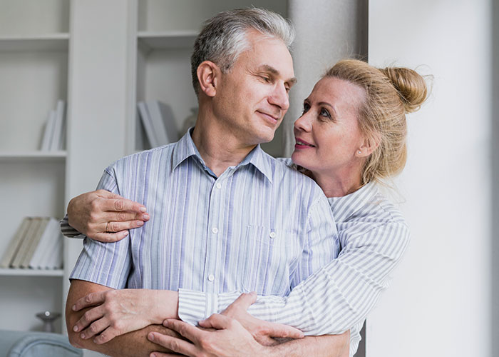 Older couple embracing and smiling affectionately in a cozy living room setting, highlighting relationship stories.